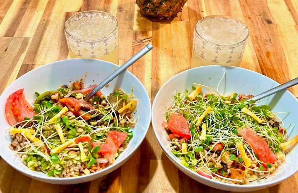 Two grain bowls topped with microgreens, tomato, and cheese