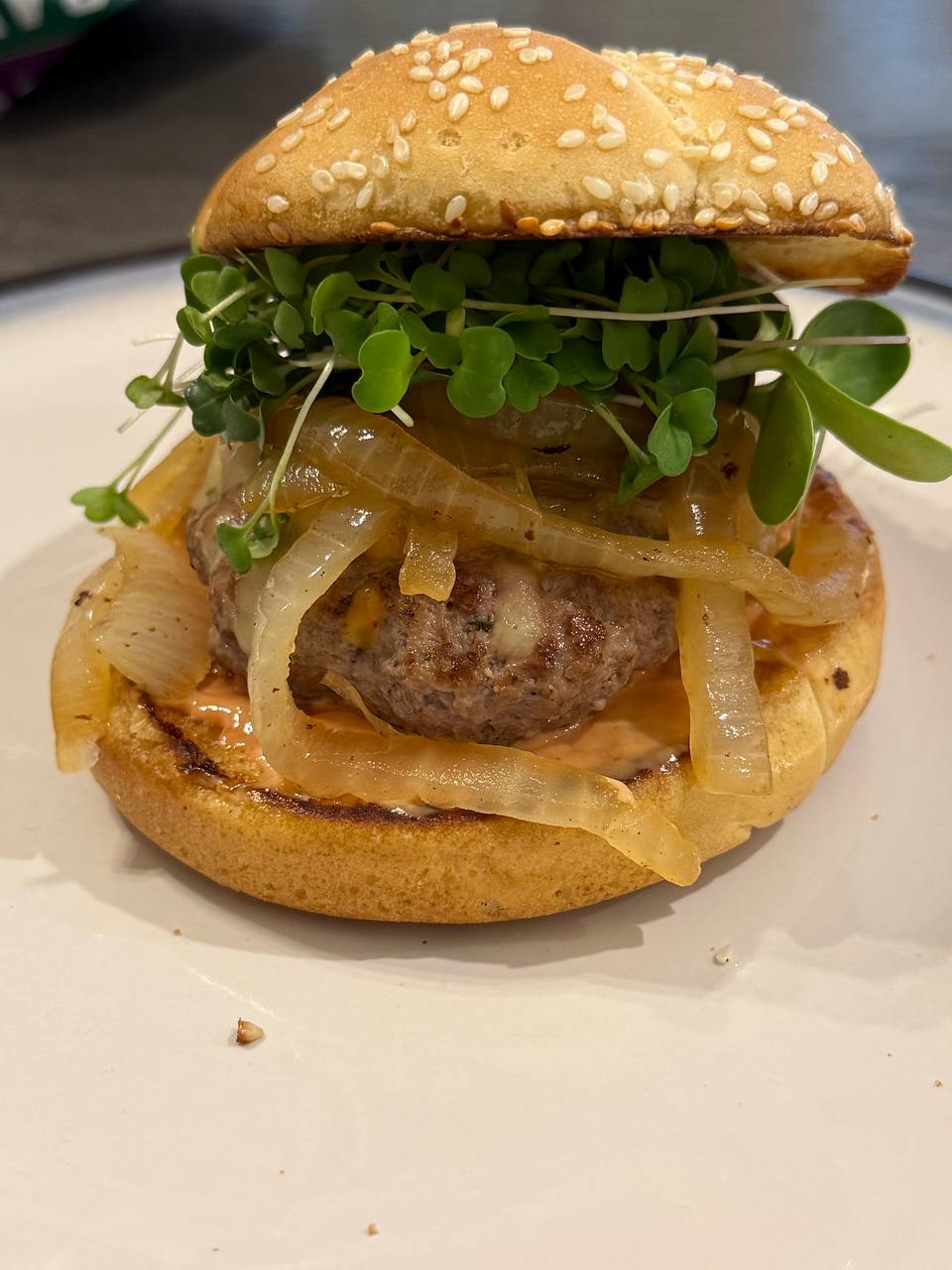 A burger with caramelized onions topped with microgreens