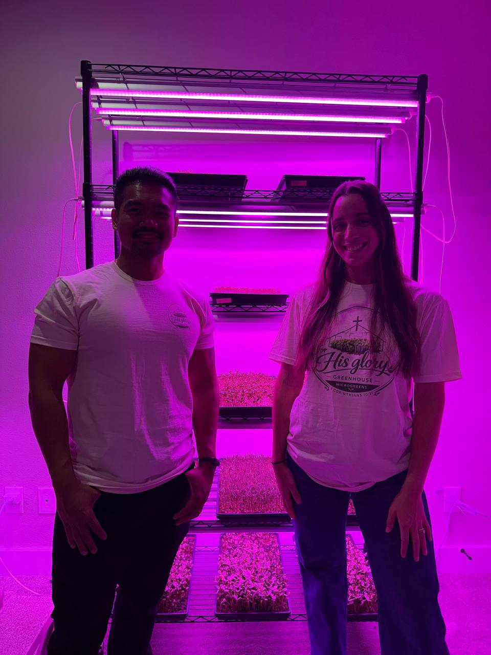 The two founders of For His Glory Greenhouse smiling in front of their grow rack