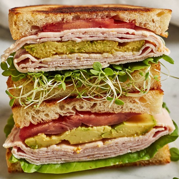 A stacked turkey and avocado sandwich layered with microgreens